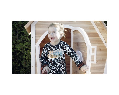 Enfant souriant devant une cabane de jeu en bois avec porte