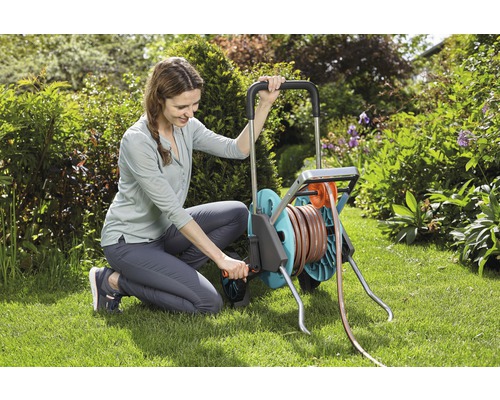 Femme utilisant un chariot de tuyau d''arrosage dans le jardin.