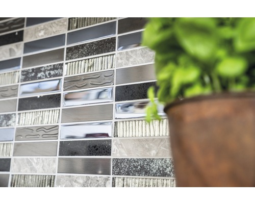 Gros plan d''un mur avec des carreaux de mosaïque dans différentes nuances de gris, à côté d''une plante