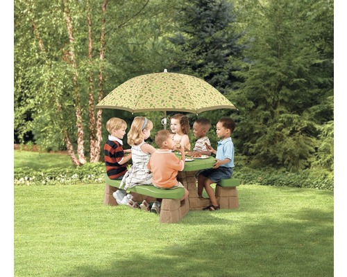 Des enfants sont assis à une table de pique-nique avec un parasol dans le jardin.