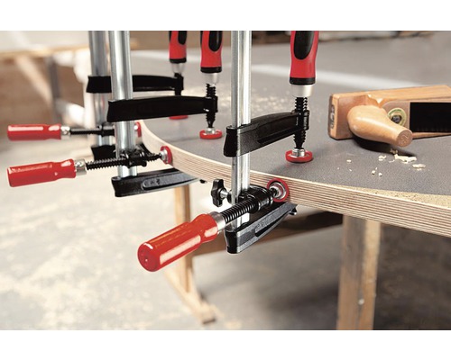 Mehrere Schraubzwingen fixieren ein Werkstück auf einer Werkbank.