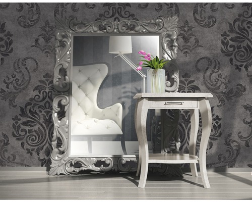 Pièce décorative avec grand miroir, fauteuil et table d''appoint devant un mur de papier peint à motifs.