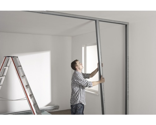 Un homme installe une ossature métallique pour une cloison sèche dans une pièce.