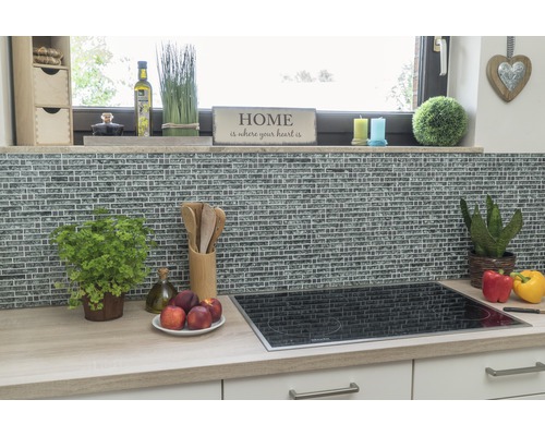 Scène de cuisine avec mur en mosaïque, plaque de cuisson et ustensiles de cuisine sur un plan de travail.