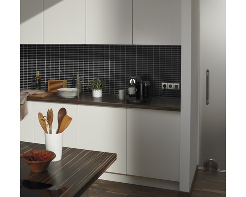 Küchenansicht mit Arbeitsplatte, Küchenutensilien und Elektrogeräten vor einer Mosaikfliesenwand