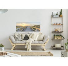 Wohnzimmer mit Sofa, Regal und einem Wandbild mit einem Weg zum Strand bei Sonnenuntergang