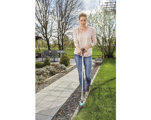 Une femme utilise un coupe-bordures dans le jardin pour tailler les bordures de la pelouse.