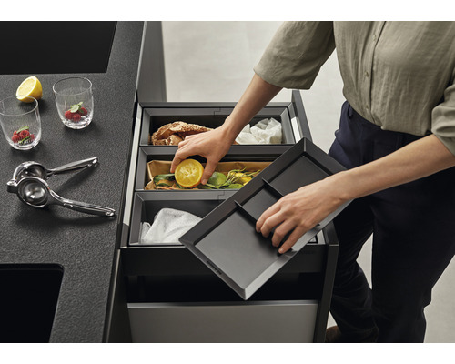 Système de tri des déchets avec plusieurs bacs dans une cuisine moderne, personne jetant des déchets