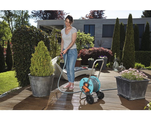 Frau bewässert Pflanzen mit einem Gartenschlauch auf einer Schlauchtrommel im Garten.