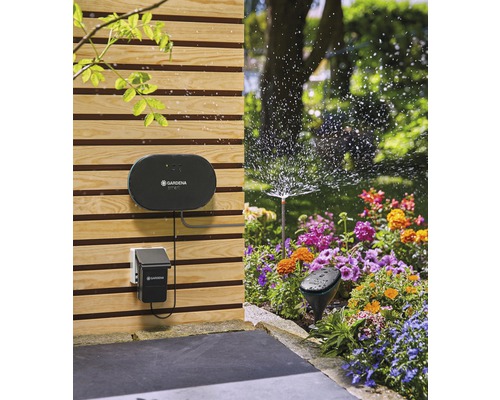 Szene mit dem Bewässerungssystem von Gardena mit Bewässerungscomputer, Sensor und Sprinkler in einem Garten mit Blumenbeet