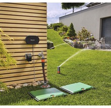 Scène d''un jardin avec un système d''irrigation, comprenant des arroseurs escamotables et des dispositifs de commande sur un mur en bois.