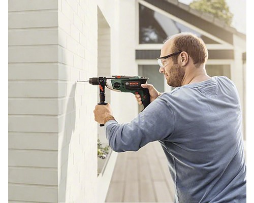 Un homme perce un trou dans un mur avec une perceuse à percussion.