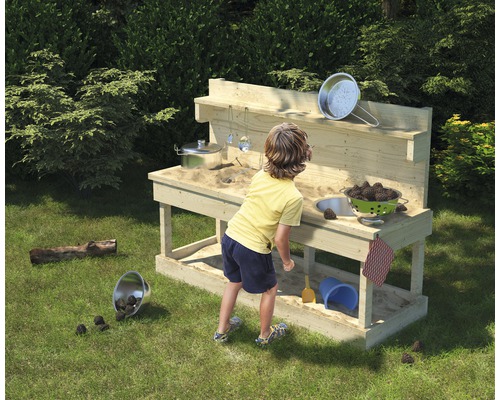 Enfant jouant avec une cuisine de boue dans le jardin.