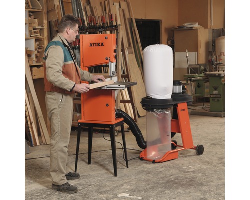 Un homme utilise une scie à ruban Atika dans un atelier. Bois et outils en arrière-plan.
