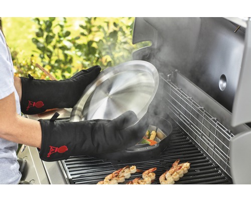 Person grilliert Crevetten und Gemüse mit Grillhandschuhen und Grillpfanne auf einem Grill.