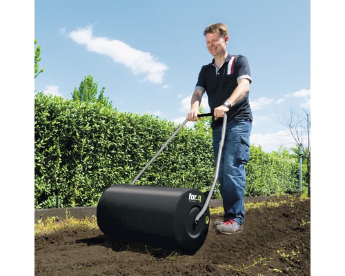 Un homme utilise un rouleau à gazon de for.q dans le jardin.
