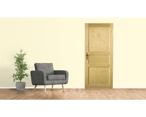 Holzzimmertür mit drei Feldern neben Sessel und Topfpflanze