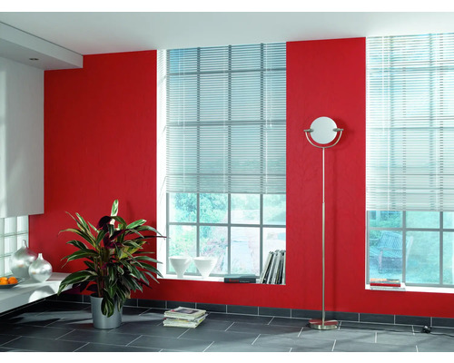 Helles Zimmer mit zwei Fenstern, ausgestattet mit Jalousien, roter Wand und Stehlampe