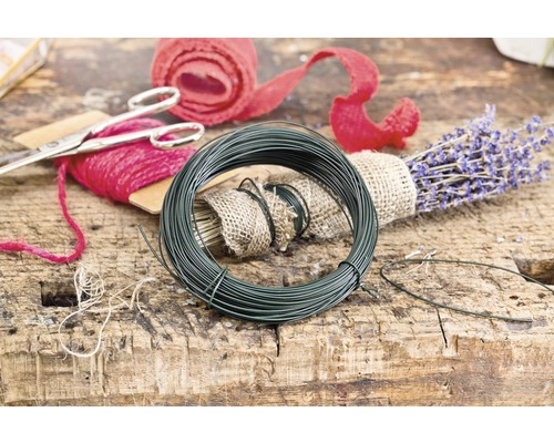 Rolle grüner Blumendraht neben Lavendel und Geschenkband auf einem Holztisch