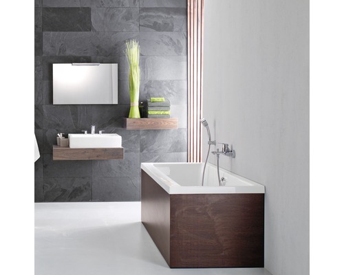 Salle de bains avec baignoire, lavabo, miroir et étagères devant un mur en pierre grise