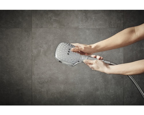 Pomme de douche avec flexible de douche dans les mains devant des carreaux muraux