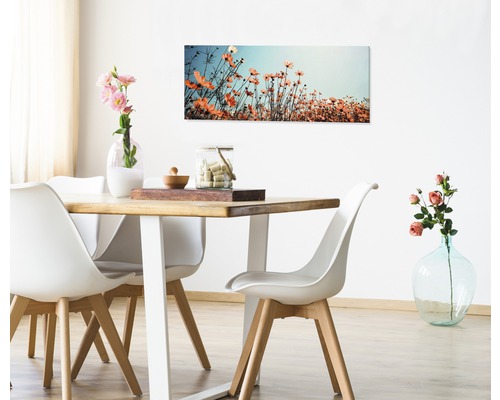 Salle à manger avec table en bois, chaises blanches et tableau de fleurs au mur