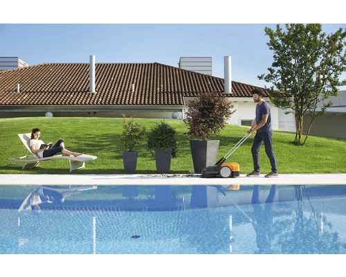 Scène avec une personne utilisant une tondeuse à gazon au bord de la piscine, tandis qu''une autre personne se détend sur une chaise longue.