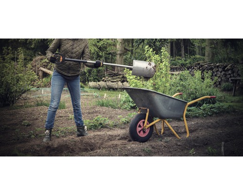 Une personne remplit une brouette dans le jardin avec une pelle.