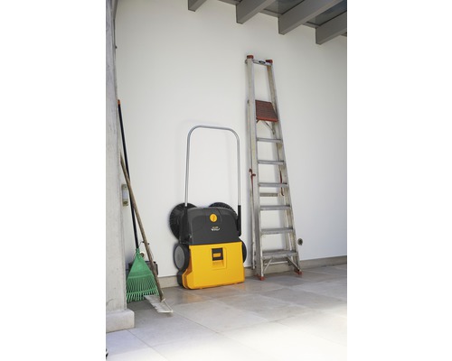Balayeuse, échelle et balais appuyés contre un mur.