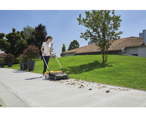 Une femme balaie les feuilles avec une balayeuse dans le jardin.