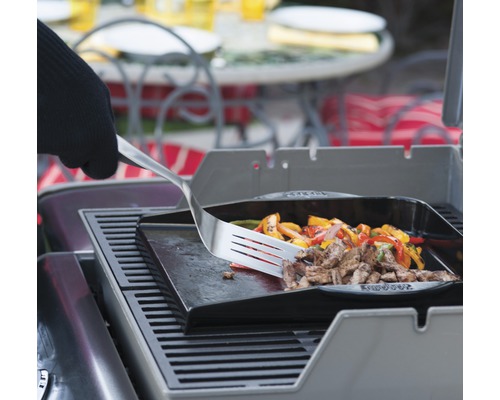 Grillplatte mit Fleisch und Gemüse wird mit einem Pfannenwender gewendet.