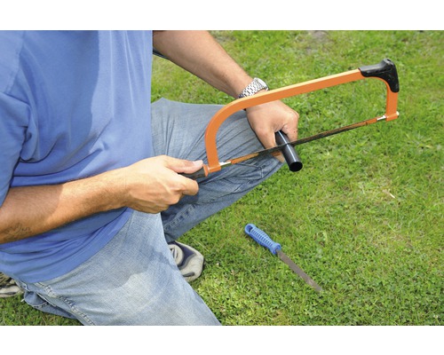 Mann sägt ein Rohr mit einer Metallsäge, eine Feile liegt im Gras.