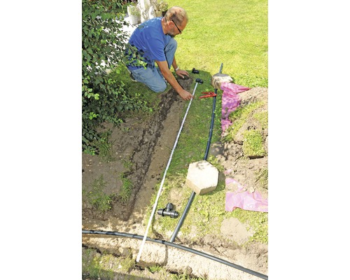 Mann misst Bewässerungssystem im Garten mit Zollstock.