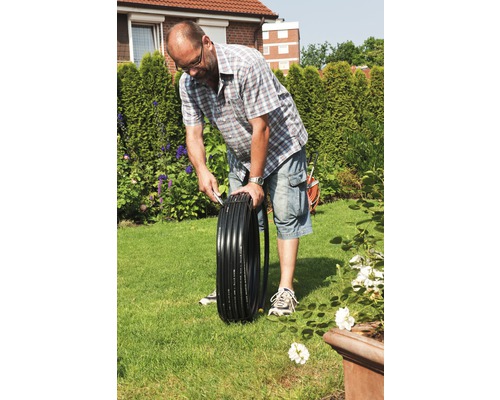 Eine Person rollt einen schwarzen Bewässerungsschlauch im Garten aus.