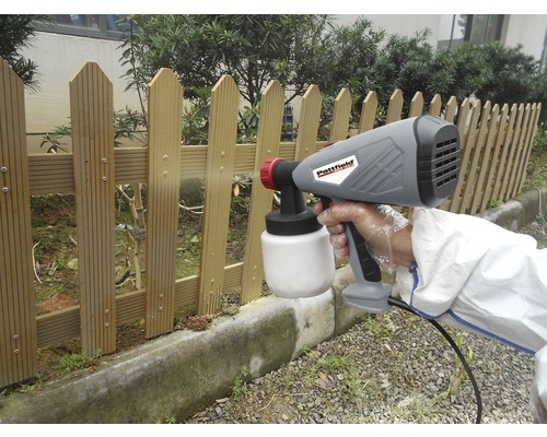 Une personne utilise un pistolet à peinture pour peindre une clôture en bois.