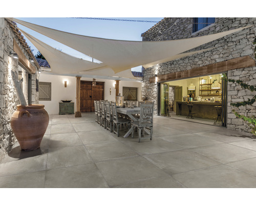 Aussenbereich mit Steintisch, Stühlen und Bodenfliesen unter einem Sonnensegel.