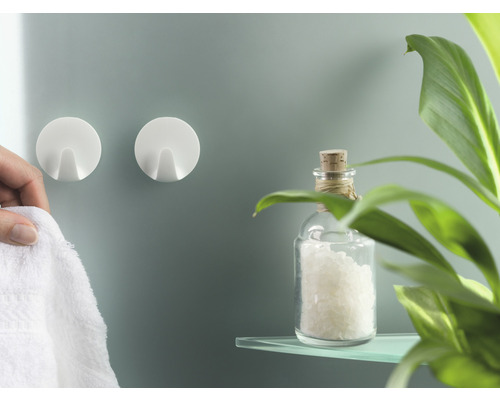 Deux crochets adhésifs ronds blancs sur un mur de salle de bains, avec une serviette et décoration