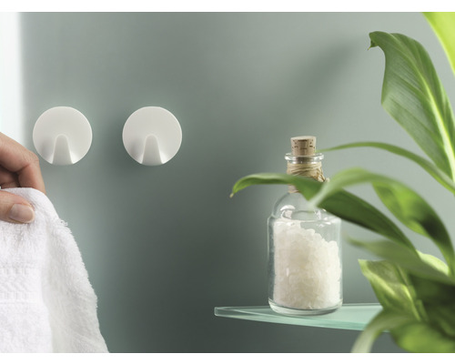 Deux crochets muraux ronds et une personne y accrochant une serviette, ainsi qu''une bouteille en verre et une plante sur une étagère