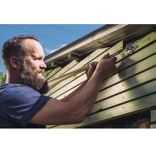 Mann befestigt eine Ladungssicherung an einem Holzschuppen