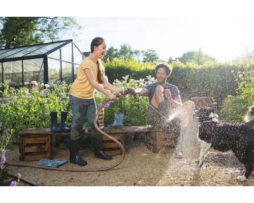Scène de jardin avec enfant, homme et chien jouant avec un tuyau d''arrosage.