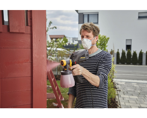 Homme peignant du bois avec un système de pulvérisation de peinture et un masque respiratoire