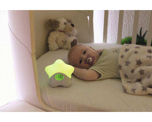 Baby liegt im Kinderbett mit Nachtlicht in Sternform, das die Temperatur anzeigt