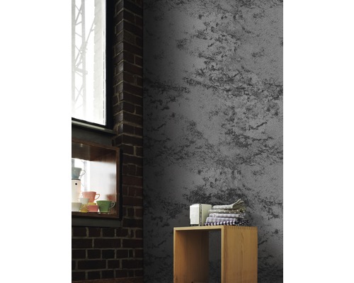 Graue Wandtapete mit rauem Putzmuster in einem Zimmer mit Backsteinmauer und Holzregal.