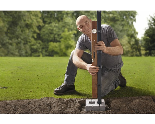 Mann richtet Holzpfosten mit Wasserwaage und Pfostenträger im Garten aus.