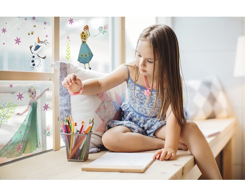 Fille assise près de la fenêtre avec des stickers muraux La Reine des neiges, des crayons et du papier