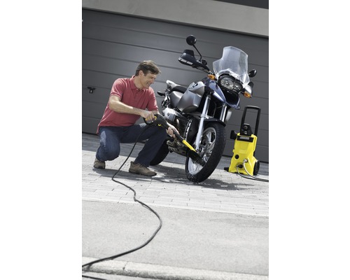 Un homme nettoie une moto avec un nettoyeur haute pression devant un garage