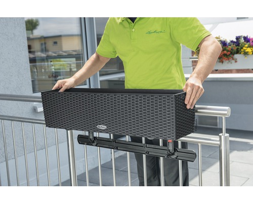 Une personne fixe une jardinière de couleur foncée avec support à une balustrade.