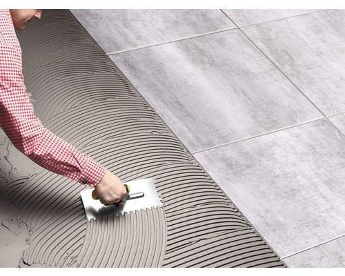 Un homme pose des carreaux à l''aide d''une spatule pour répartir la colle à carrelage