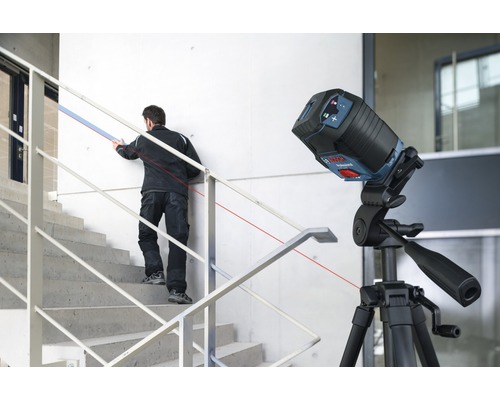 Chantier avec laser linéaire sur trépied et artisan sur escalier