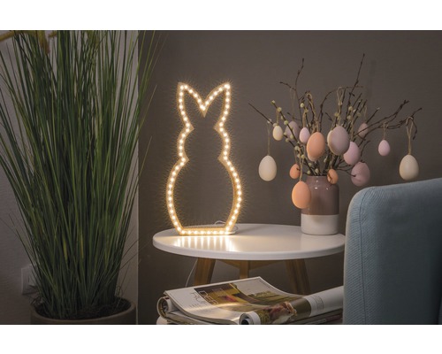 Dekorative Szene mit einer beleuchteten Hasenfigur, Ostereiern und einer Zimmerpflanze auf einem Tisch